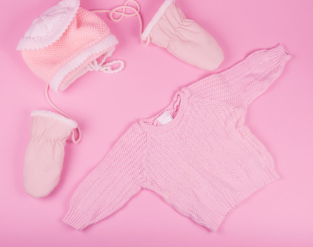 Baby hat, mittens and sweater of pink color on a pastel pink background (top view, retro style)の写真素材