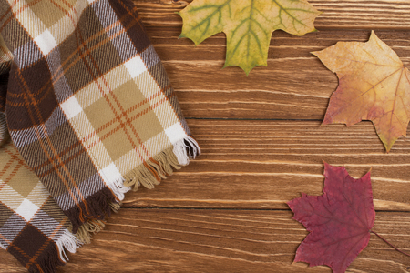 Cozy checkered scarf and autumn maple leaves on a wooden background, top view (copy space in the center)の写真素材