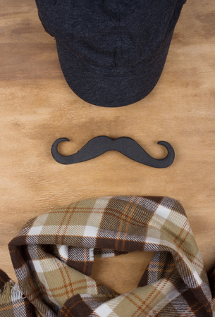 Cap, black moustache and checkered scarf on a wooden background (top view), menswear conceptの写真素材