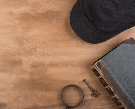 Cap of a detective, an old book, a key and a magnifying glass against a worn wooden background (top view, copy space on the left for your text) as the detective or crime story conceptの写真素材
