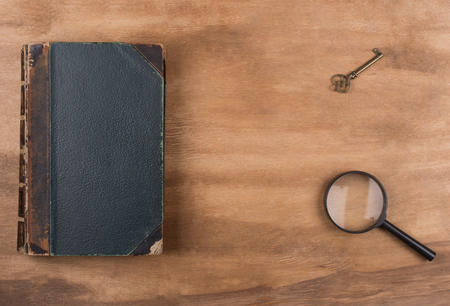 Old book, a key and a magnifying glass against a worn wooden background (top view, copy space in the center for your text) as the crime story conceptの写真素材
