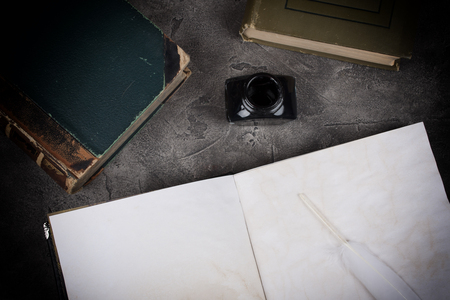 Old books, an open old diary with blank pages, a white feather as a quill pen and an inkwell on a gray marble background with dark edges (top view), retro styleの写真素材