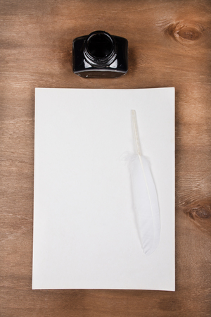 Inkwell and a blank old sheet of paper with a white feather as a quill pen on a worn wooden background (top view)の写真素材