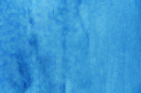 Blue frost pattern on the window glass with sparkles (as a beautiful festive New Year or winter background)の写真素材