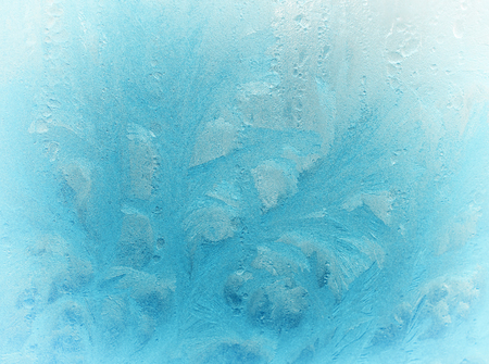 Fantastic fairy-like light blue frost pattern on the window glass (as an abstract winter background), retro toned with a faded film effectの写真素材