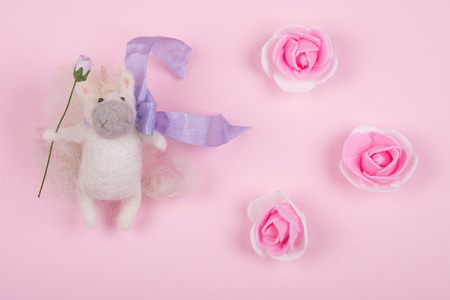 Tiny unicorn toy made of wool and handmade rose buds on a pastel pink background (top view), copy spaceの写真素材