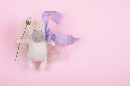 Tiny handmade unicorn toy decorated with a ribbon and holding a flower (copy space on the right)の写真素材