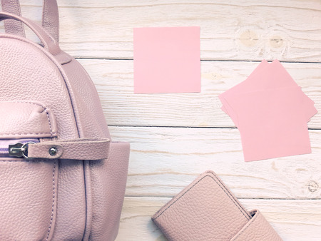 Top view of a pink backpack, pink wallet and blank pink paper cards on a wooden background (retro toned)の写真素材