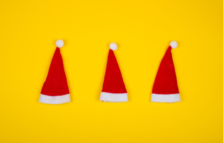 Three small Santa hats on the bright yellow background as the Christmas concept (top view, minimal style)の写真素材