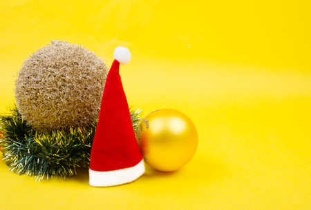 Small Santa hat, golden Christmas balls and a Christmas wreath on the bright yellow background as the Christmas concept (copy space on the right for your text)の写真素材