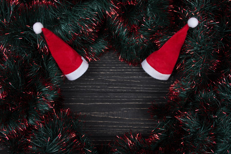Two Santa hats and green and red tinsel forming a frame on a black wooden background as a New Year or Christmas background (top view, copy space in the center for your text)の写真素材