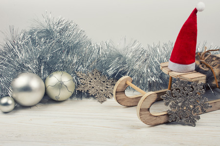 Christmas or New Year decorations (wooden toy Christmas sleigh with a Santa hat, silver tinsel, snowflakes and Christmas balls on a white wooden background), copy space for your text, retro styleの写真素材
