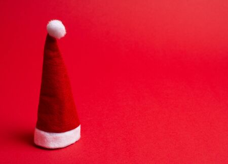 Santa hat on the bright red background as the Christmas concept (minimal style), copy space on the right for your textの写真素材