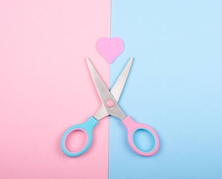 Open pink and blue scissors ready to cut a paper heart on the pink and blue background (end of love or broken heart concept)の写真素材