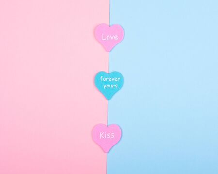 Three paper hearts with the words Love, Forever Yours and Kiss on a split pink and blue background...