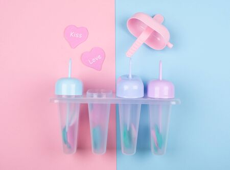 Multicolored ice cream moulds and paper hearts with the words Kiss and Love on a split pink and blue background (top view)の写真素材