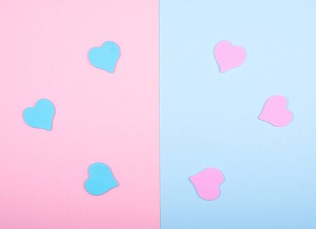 Blue and pink paper hearts on a split pink and blue background (top view, minimalist style)