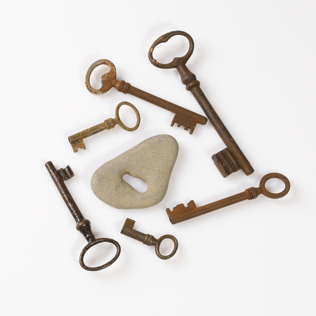 set of old rusty keys placed around gray stone with key hole on white backgroundの写真素材