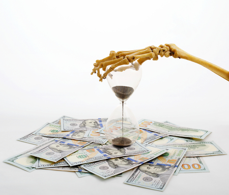 skeleton fingers holding sand-glass placed on dollars. concept of time - money and death.の写真素材