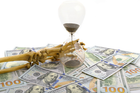 skeleton fingers holding sand-glass placed on dollars. concept of time - money and death.の写真素材