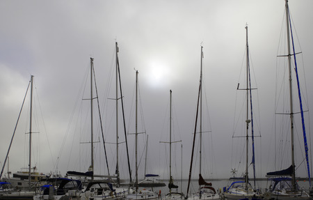 Morning fog in the seaport in Nida, Lithuania. Yacht masts in grey sky with sun disc.の写真素材