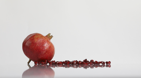 Fresh ripe pomegranate fruit and seeds on white reflective surface and white background. Front view with space for your text.の写真素材