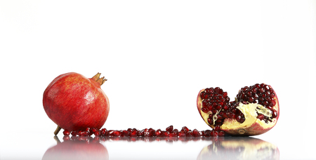 Fresh ripe pomegranate fruits and seeds on white reflective surface and white background. Front view with space for your text.の写真素材