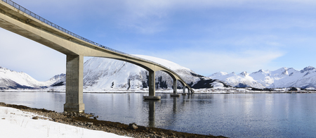 Wide panoramic view of bridge in the Lofoten islands in winter with mountains reflection in fjord.の写真素材
