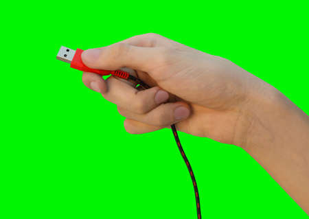 Close up male hand holding red usb cable for PC and mobile devices isolated on green background, concept of communicationの写真素材
