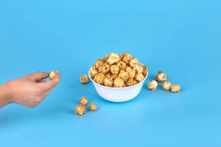 A child's hand from the side takes popcorn from the plate. Free space, blue background. The concept...