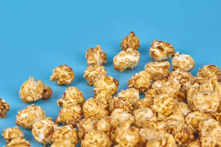 Large popcorn grains casually scattered on a blue background close-up. Sweet corn in caramel glaze....