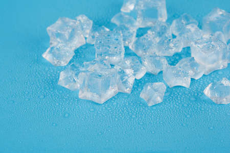 Whole ice cubes and shards of ice lie in melt water on a blue background. Free space