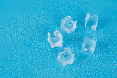 Five ice cubes on a blue background in water dropsの写真素材