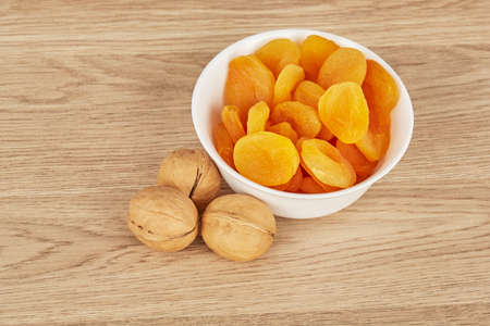 White bowl of dried apricots on a wooden background with three walnutsの写真素材