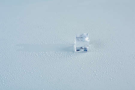 An ice cube glides across a gray background in drops of meltwater