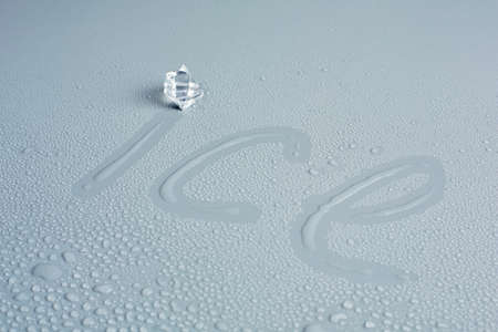Inscription ice on a gray background and one ice cubeの写真素材