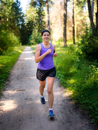 Girl in purple shirt runs into the woods. A healthy lifestyle. Training for a marathon.の写真素材