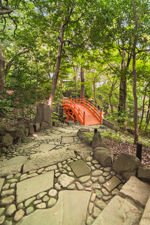 Spiral staircase paved with stones and pebbles leading to the Japanese vermilion Tsuten bridge surrounded by maples and cherry trees in the forest of Koishikawa Korakuen Park.のeditorial素材