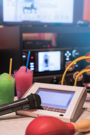 Black microphone in karaoke club, with remote controller, melon and strawberry soda drinks, yellow drum and screen for singing music on stage party.の写真素材