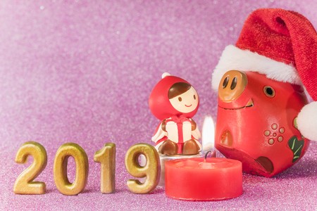 Pink glitter background for New Year's Cards with funny figurines of two boars  and chid with a Christmas hat dancing around a candle and handmade golden numbers of 2019 year.の写真素材