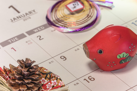 Japanese New Year's ornament with pine cone and cute Japanese Zodiac animal figurines of boar on a Japanese calendar open on 2019 January page.の写真素材