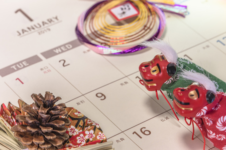 Japanese New Year's ornament with pine cone and cute Japanese folklore animals figurines of lions Shishimai on a Japanese calendar open on 2019 January page.の写真素材