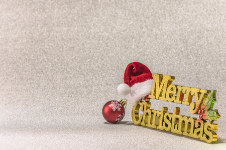 Santa Claus hat put on a golden word Merry Christmas with a Christmas Tree snowflakes pattern ornament ball on a glitter silver snow background.の写真素材