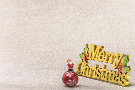Cute tiny figurine of Santa Claus on a Christmas tree snowflakes pattern ornament ball with a glitter silver snow background and the golden words Merry Christmas.の写真素材