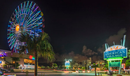 Naha, Japan - September 16, 2018: Night view of the Mihama Carnival Park Ferris wheel located in the American Village neighborhood of Naha City decorated with palm trees near Sunset Beach in Okinawa.のeditorial素材