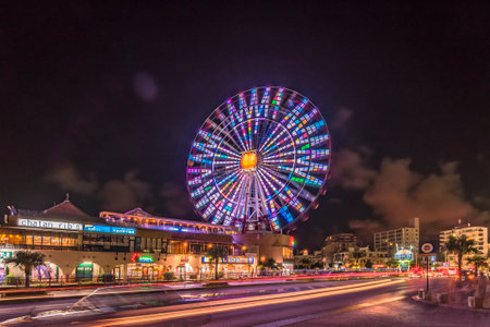 Naha, Japan - September 16, 2018: Night view of the Mihama Carnival Park Ferris wheel located in the American Village neighborhood of Naha City decorated with palm trees near Sunset Beach in Okinawa.のeditorial素材