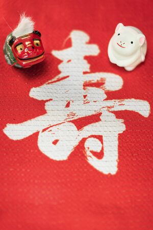 A Japanese greeting card with a cute rat figurine for the 2020 year of the mouse and a Folklore animal figurine depicting a Shishimai lion on a red cloth decorated with the Japanese Kotobuki ideograph which means longevity.の写真素材