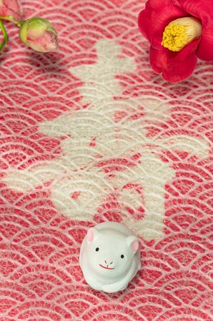 A Japanese greeting card with a Tsubaki flower also called the winter rose and a cute rat figurine for the 2020 year of the mouse on a red cloth decorated with the Japanese Kotobuki ideograph which means longevity.の写真素材