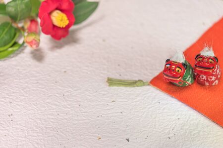 A Japanese greeting card with a Tsubaki flower also called the winter rose and two Folklore animals figurines depicting two Shishimai lion on a on an orange pillow on a white crumpled paper whith gold and silver fragments.の写真素材