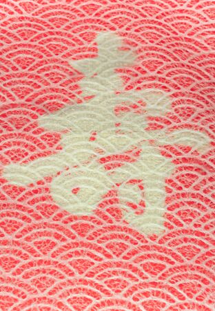 A Japanese greeting card with a traditional lace circles motif pattern on a red cloth decorated with the Japanese Kotobuki ideograph which means longevity.の写真素材